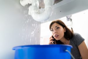 woman-looks-under-sink-at-leaking-pipes-while-on-phone